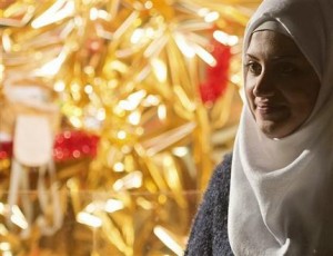 In this photo taken Tuesday, Dec. 8, 2015, Syrian refugee Reem Habashieh stands in front of a golden decoration of one of the illuminated sales booths at the Christmas market in Zwickau, eastern Germany. Her Muslim family with mother Khawla Kareem, one sister and two brothers has joined in the Christmas spirit of their neighbors, decorating the door of their flat with glittery red bells and tree branches in green and gold. (AP Photo/Jens Meyer)